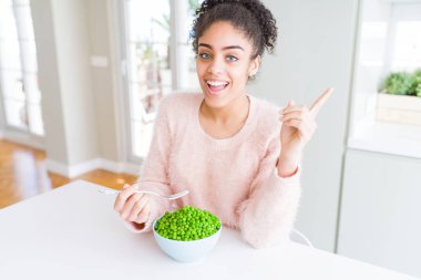 Sağlıklı yeşil bezelye yeme genç Afrikalı Amerikalı kız yan el ve parmak ile işaret çok mutlu