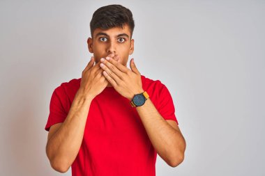 İzole edilmiş beyaz arka planın üzerinde duran kırmızı tişörtlü genç Hintli adam yanlışlıkla ağızlarını kapatarak şok geçirdi. Gizli konsept.
