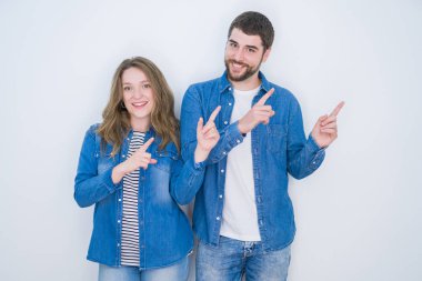 Genç güzel çift beyaz izole arka plan üzerinde birlikte ayakta gülümseyerek ve yan iki el ve parmakları ile işaret kamera bakıyor.