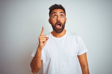 İzole beyaz arka plan üzerinde duran t-shirt giyen genç hintli adam başarılı bir fikir ile parmak işaret. Çıktı ve mutlu. Bir numara.