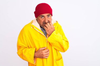 İzole edilmiş beyaz arka planda duran yağmurluk ve yün şapka giyen orta yaşlı bir adam elleri ağız yiyen tırnaklarla stresli ve gergin görünüyor. Endişe sorunu.