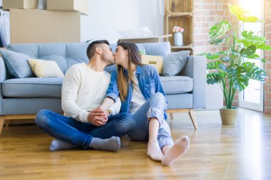 Yeni bir daire zemin üzerinde oturan genç güzel çift, yeni bir eve taşınmak için mutlu sevgi gülümsüyor