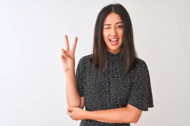 Zarif bir tişört giyen genç Çinli kadın izole edilmiş beyaz arka planda dikiliyor ve kameraya gülümsüyor zafer işareti yapıyor. İki numara..