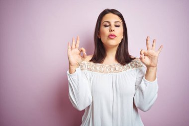 Pembe izole edilmiş arka planda genç, güzel esmer kadın rahatla ve parmaklarıyla meditasyon hareketi yaparken gözleri kapalı gülümse. Yoga konsepti.