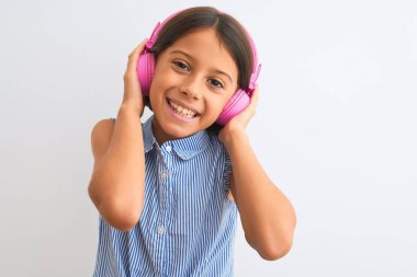 Güzel kız müzik dinliyor, kulaklık takıyor, beyaz arka planda mutlu bir yüz takıyor, gülümsüyor ve kendine güvenen bir gülümsemeyle dişlerini gösteriyor.