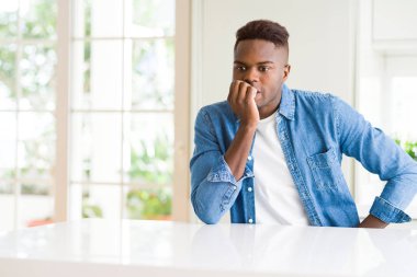Yakışıklı afro-amerikan adam evde stresli ve gergin görünüyor elleri ağzında ve tırnaklarını yiyor. Endişe sorunu.