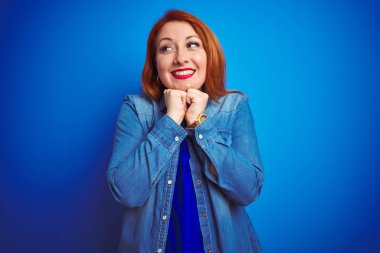 Genç, kızıl saçlı, güzel bir kadın. Kot gömlek giyiyor. Mavi izole arka planda duruyor.