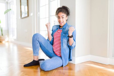 Afro saç ile güzel genç Afrikalı Amerikalı kadın yerde oturan sürpriz kutluyor ve silah ile başarı için hayran kaldırdı ve açık gözler. Kazanan kavramı.