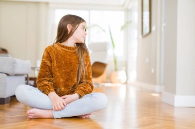 Güzel genç kız çocuk evde yan bakarak katta oturan, kendine güvenen gülümseme ile doğal yüzü ile profil poz rahatlayın.