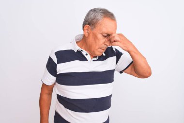 İzole edilmiş beyaz arka planda duran sıradan çizgili polo giyen yaşlı gri saçlı adam yorgun burnu ve gözleri ovuşturup yorgunluk ve baş ağrısı hissediyordu. Stres ve hüsran kavramı.