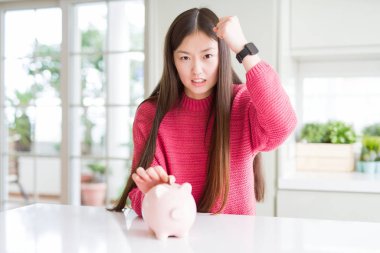 Güzel Asyalı kadın domuz çantasına bozuk para koyuyor öfkeyle bağırıyor, çıldırıyor ve bağırıyor.