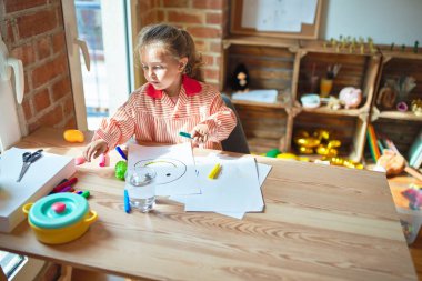 Güzel sarışın kız okul üniforması giyiyor. Anaokulunda renkli kalemlerle resim çiziyor.