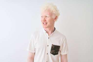 Genç albino sarışın, günlük gömlek giyen, izole edilmiş beyaz arka planda duran, yüzünde gülümseme ve doğal ifadeyle yan yana bakan bir adam. Kendinden emin gülen.