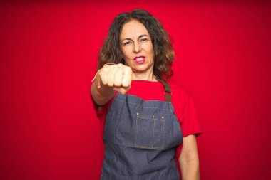 Kırmızı arka planda önlük giyen orta yaşlı bir kadın yumruk yumruğa dövüşmek, agresif ve öfkeli saldırı, tehdit ve şiddet.