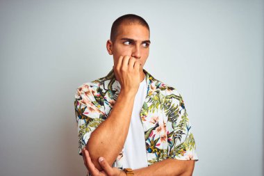 Tatilde beyaz arka planda Hawaii tişörtü giyen yakışıklı genç adam elleri ağız yiyen tırnaklarla gergin ve stresli görünüyor. Endişe sorunu.