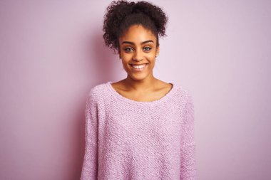 Kış süveteri giyen genç Afro-Amerikan kadın mutlu ve havalı bir gülümsemeyle izole edilmiş pembe arka planda dikiliyor. Şanslı kişi..