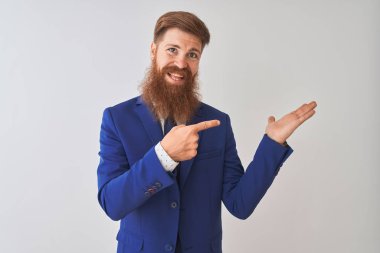 İzole edilmiş beyaz arka plan üzerinde duran genç, kızıl saçlı iş adamı kameraya hayret ediyor ve gülümsüyor..