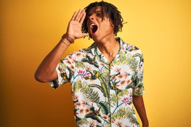 Tatilde saçı rastalı bir Afro adam izole edilmiş sarı arka planda tişört giyiyor ve el ele tutuşarak bağırıyor. İletişim konsepti.