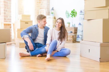 Evde karton kutular etrafında yerde oturan rahatlatıcı genç güzel çift, yeni bir eve hareket mutlu gülümseyen