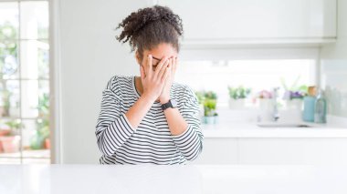 Afro saçlı, sıradan çizgili süveter giyen, suratını ellerle örten ve ağlayan güzel Afro-Amerikan kadını. Depresyon kavramı.