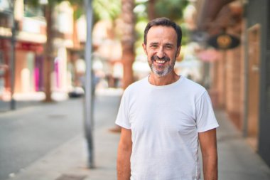 Orta yaşlı yakışıklı adam sokakta gülümsüyor.