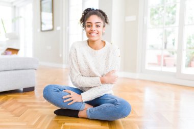 Afro saçlı güzel genç Afrikalı Amerikalı kadın kamera bakarak çapraz silah ile gülümseyen katta mutlu yüz oturuyor. Pozitif kişi.