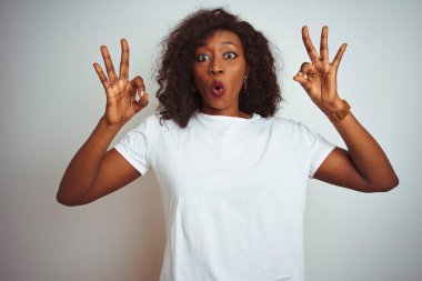 İzole edilmiş beyaz arka planda duran tişört giyen genç Afro-Amerikalı kadın şaşırmış ve şok olmuş bir şekilde parmaklarıyla onay sembolü çiziyor. Çılgın ifade