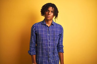 Rastgele gömlek giyen, izole edilmiş sarı arka planda duran Afro adam yüzünde ciddi bir ifadeyle rahatlamış. Basit ve doğal bir şekilde kameraya bakıyorsun..