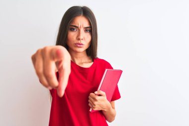 Genç ve güzel bir kız öğrenci elinde kırmızı bir kitapla izole edilmiş beyaz arka planda kamerayı işaret ediyor ve sen, el işareti, ön taraftan pozitif ve kendinden emin bir jest.