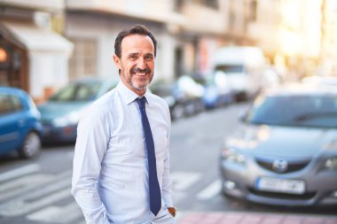 Orta yaşlı yakışıklı işadamı tişört ve kravat takıp sokakta gülümsüyor.