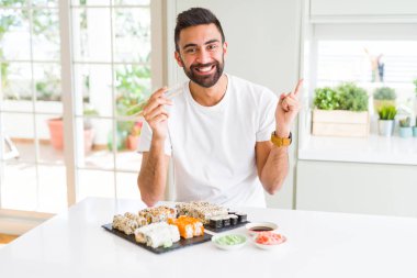 Chopsticks kullanarak Asya Suşi yeme yakışıklı İspanyol adam çok mutlu yan el ve parmak ile işaret