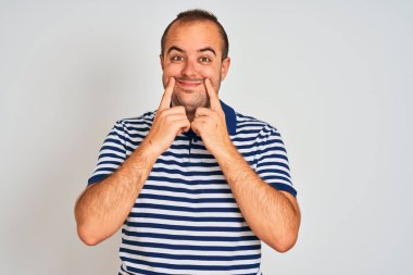 Sıradan çizgili polo giyen genç adam izole edilmiş beyaz arka planda duruyor ağzı açık gülümsüyor, parmakları işaret ediyor ve neşeli bir gülümseme sergiliyor.