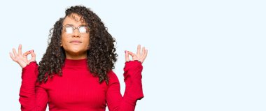 Gözlük sakin ol kıvırcık saçlı Genç güzel kadın ve gülümseyen gözlerle parmak ile meditasyon jest yapıyor kapalı. Yoga kavramı.