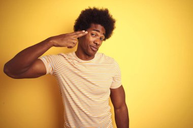 Afro saçlı, çizgili t-shirt giyen Amerikalı bir adam izole edilmiş sarı arka planda duruyor. Kendini vuruyor ve öldürüyor..