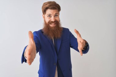 Genç, kızıl saçlı, takım elbiseli bir iş adamı izole edilmiş beyaz arka planda kameraya sarılıp gülümsüyor. Mutluluğu kucaklayan neşeli bir ifade..