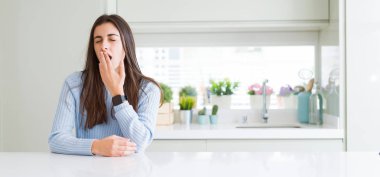 Evde beyaz masada oturan güzel genç kadının geniş açılı resmi el ile ağız kapatarak yorgun esneme sıkılmış. Huzursuz ve uykululuk.