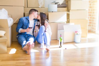 Karton kutular etrafında yeni evin katında oturan genç çift, şarap bir bardak içme kutluyor ve yeni daire için mutlu gülümseyen