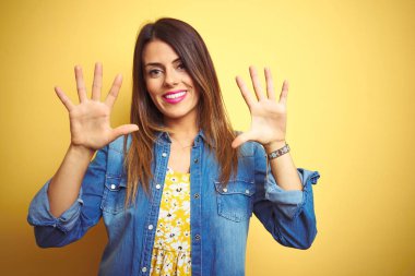 Sarı arka planda duran genç ve güzel bir kadın on numarayı gösterip işaret ederken kendinden emin ve mutlu bir şekilde gülümsüyor..