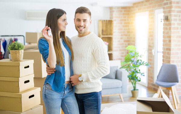 Young couple moving to a new home, hugging in love showing keys of new apartment smiling very happy