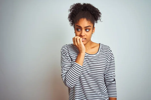 African american woman wearing navy striped t-shirt standing over isolated white background looking stressed and nervous with hands on mouth biting nails. Anxiety problem.