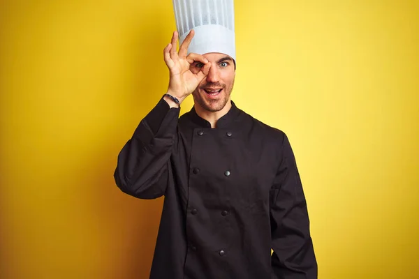 年轻的厨师 身穿制服 头戴一顶帽子 站在孤立的黄色背景上 做着一个手势 脸上挂着微笑 眼睛看着手指 面带笑容 — 图库照片
