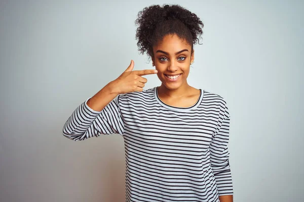 African american woman wearing navy striped t-shirt standing over isolated white background Pointing with hand finger to face and nose, smiling cheerful. Beauty concept