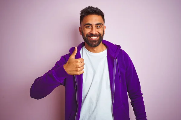 年轻的印度男子穿着紫色运动衫 站在孤立的粉色背景上 手举着快乐的大拇指 在镜头前看着成功的表情 — 图库照片