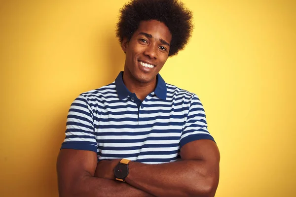 American man with afro hair wearing navy striped polo standing over isolated yellow background happy face smiling with crossed arms looking at the camera. Positive person.