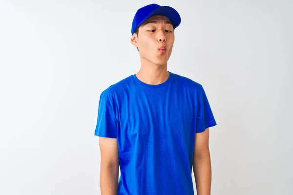 青いTシャツとキャップを身に着けている中国の配達人は 狂気とコミカルなジェスチャーで魚の顔を作る孤立した白い背景の上に立っている 面白い表現 — ストック写真