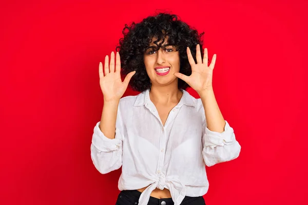 年轻的阿拉伯女人 卷曲的头发 身穿白色休闲衫 披着孤立的红色背景 带着自信和快乐的笑容 用手指指点着十号 — 图库照片