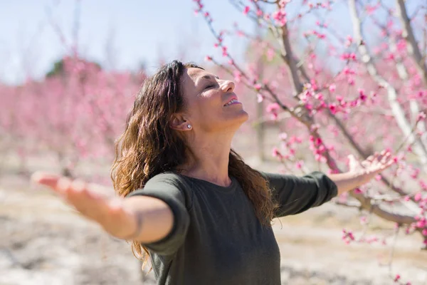 Bella donna di mezza età nel mezzo di fiori di pesca rosa a — Foto Stock