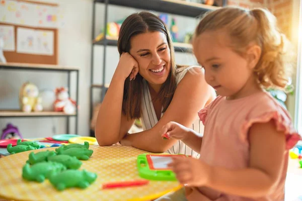 Beautiful teacher and blond student toddler girl drawing using digital board at kindergarten