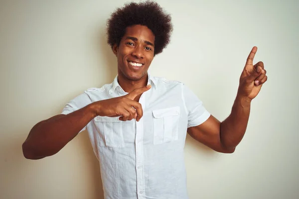 African american man with afro hair wearing shirt standing over isolated white background smiling and looking at the camera pointing with two hands and fingers to the side.
