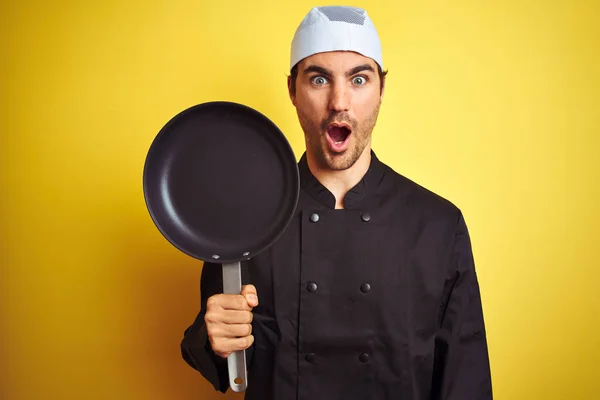 Mladý Kuchař Uniformě Klobouku Drží Pánev Izolovaném Žlutém Pozadí Vyděšený — Stock fotografie